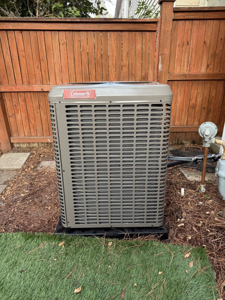 New Coleman air conditioner condenser installed beside a wood fence at a Raleigh-area home